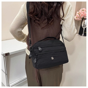 Detail view of black nylon crossbody bag featuring multiple zipper compartments and metal logo