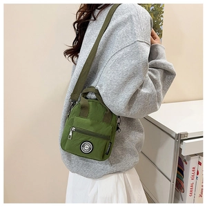 Detail of army green nylon crossbody bag with dual zipper compartments and top handle