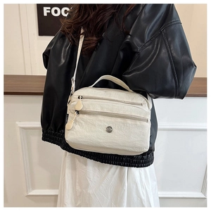 Detail view of cream nylon crossbody bag showing multiple zipper pockets and logo