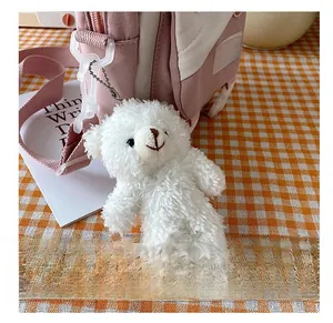 Detail showing white fluffy teddy bear charm hanging on a pink and white canvas crossbody bag