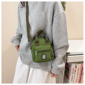 Detail of green nylon crossbody bag showing the front zipper pocket and round brand logo