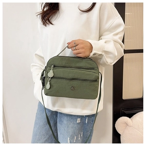 Army green multi-zipper nylon crossbody bag shown worn by a model in a lifestyle setting