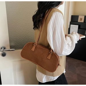 Brown suede underarm bag with gold metal hardware shown on model shoulder in warm tones