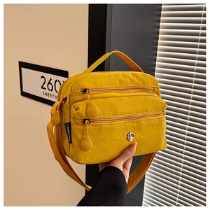 Detail view of yellow nylon crossbody bag featuring multiple zippers and smooth texture
