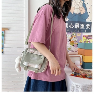 Detail view of a green canvas crossbody bag with a white plush ball charm and fashion label