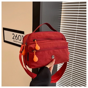 Close-up of a red nylon crossbody bag with three zipper pockets and orange pullers
