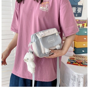 Close-up of color-block canvas crossbody bag with teddy bear pendant and fashion buckle
