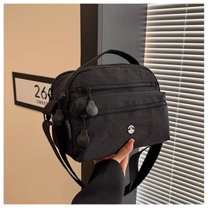 Detail of a black nylon crossbody bag with multi-zipper pockets and brand logo
