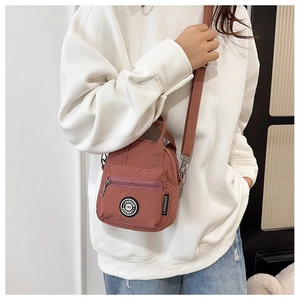 Detailed view of the brick red nylon crossbody bag showing the zipper and brand patch