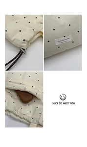 Detail of branded fabric label and metal drawstring toggle on a beige polka dot tote bag