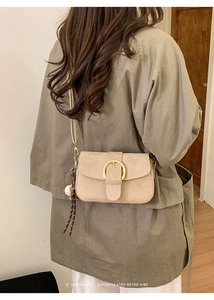 Detail of minimalist beige suede crossbody bag featuring a large gold ring buckle and charm