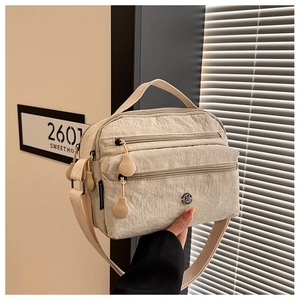 Close-up of beige nylon multi-pocket crossbody bag with zipper details and top handle