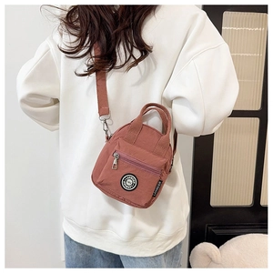 Detail of a red nylon crossbody bag with logo patch shown on a model in casual outfit