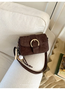 Detail of retro dark coffee suede shoulder bag with gold buckle and baseball charm