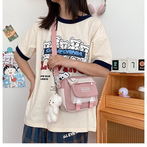 Detail of pink and white canvas crossbody bag featuring a plush bear charm and fashion label