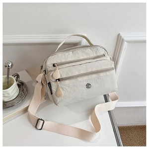 Close-up of cream nylon crossbody bag with multiple zippers and wide strap on a desk