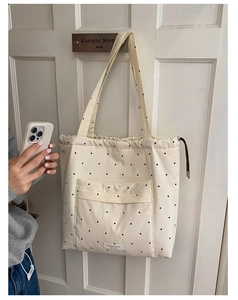 Detail of cream canvas tote bag with black polka dots featuring drawstring and front pocket