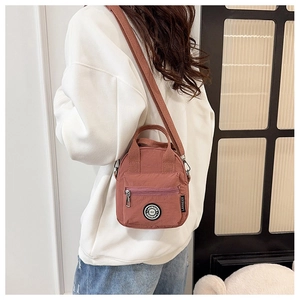 Close-up of the mauve nylon crossbody bag featuring wide woven strap and front zipper pocket