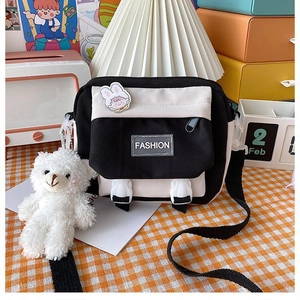 Close-up of small canvas crossbody bag with Fashion label, bear pendant and cartoon brooch