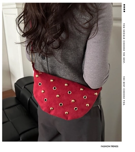 Détail du sac bandoulière en daim rouge avec clous dorés et œillets sur la bandoulière