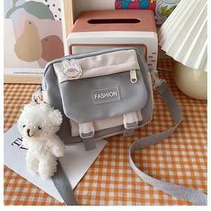 Detail of grey and beige canvas crossbody bag with fashion label and bear charm