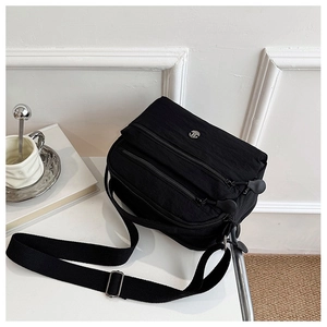 Detail of a black nylon crossbody bag with three zipper pockets and wide adjustable strap