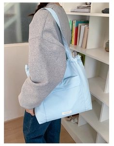 Close-up of a light blue quilted tote bag with drawstring and white brand label detail