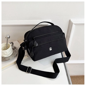 Detail of black nylon crossbody bag featuring triple front zippers and woven strap