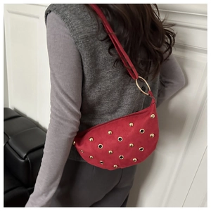 Vue détaillée du sac demi-lune en daim rouge à rivets dorés porté à l'épaule par un mannequin