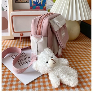 Close-up of pink and beige canvas crossbody bag featuring a cute plush bear charm accessory
