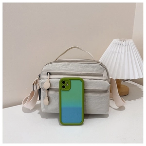 Detail view of cream nylon crossbody bag with three zipper compartments and wide strap