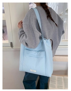 Detail of light blue drawstring tote bag showing the front pocket and logo label on the fabric