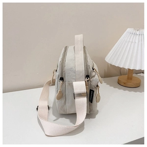 Detail view of lightweight beige nylon crossbody bag with multi-zippered compartments