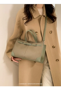 Grüne Leder-Tragetasche getragen über einem beigen Mantel in minimalistischem Retro-Stil