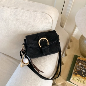 Suede matte shoulder bag with gold horseshoe buckle and baseball charm on sofa