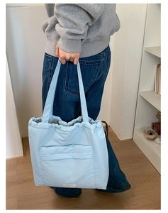 Close-up of quilted light blue tote bag showing drawstring closure and front pocket