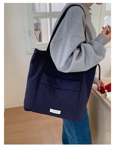Detail of navy blue tote bag showing the large front pocket and woven brand label