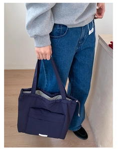Detail of navy blue nylon tote bag featuring drawstring closure and large front pocket