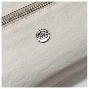 Detailed close-up of beige nylon fabric with silver M Fashion metal logo on shoulder bag