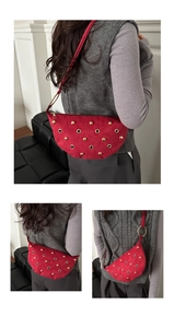 Détail du sac demi-lune en daim rouge avec rivets dorés et fermeture éclair épurée