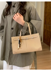 Schicke beige Strohtasche mit Perlenanhänger und Gürteldetail an elegantem Modell