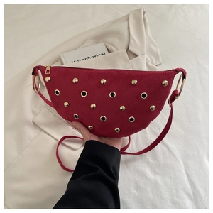Détail d'un sac demi-lune en daim rouge avec rivets dorés et œillets porté à la main