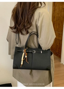 Details einer schwarzen Handtasche mit dekorativem Holzperlenanhänger und Silber-Schnalle