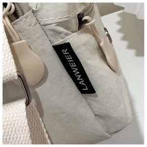 Detailed macro view of the cream nylon bag texture with zipper pocket and Lanweier tag