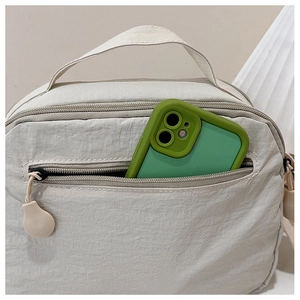 Detail view of cream nylon crossbody bag showing interior storage capacity with a phone