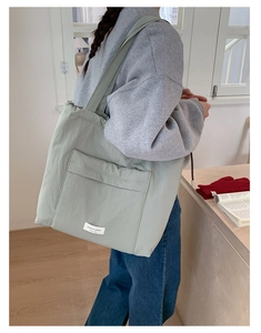 Detail of light green nylon tote bag featuring front pocket and brand woven label