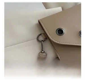 Gros plan sur pochette en cuir beige avec œillets métalliques et fermoir mousqueton