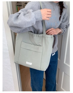 Detail of light green nylon tote bag featuring drawstring closure and front pocket