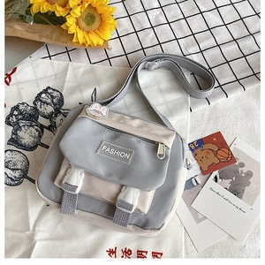 Detail of grey and beige canvas crossbody bag with buckles and fashion patch on textured background