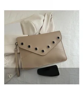 Détail d'une pochette enveloppe beige avec œillets argentés et dragonne amovible chic